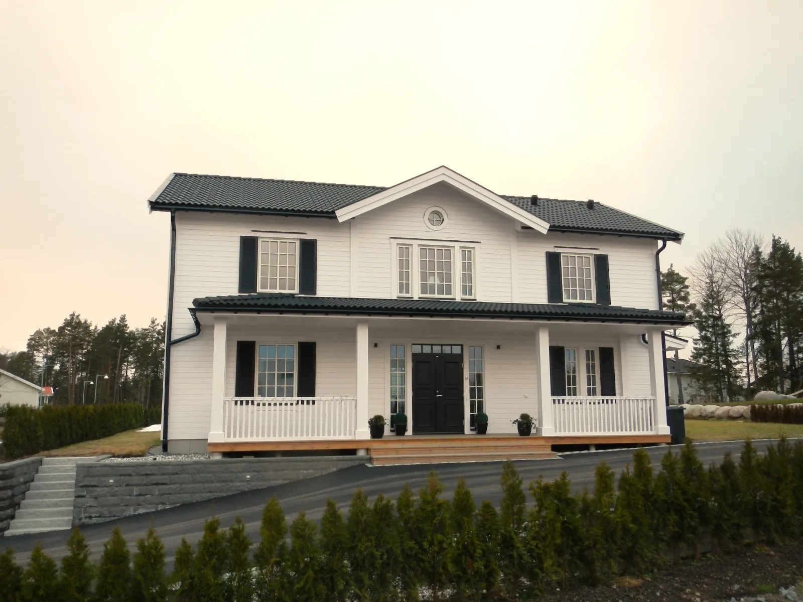 Vit villa i två plan med veranda och svarta fönsterluckor