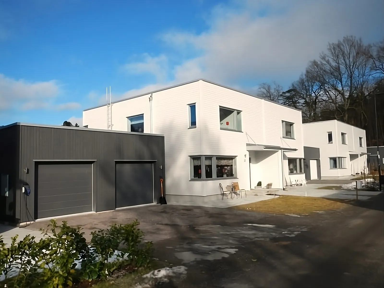 Vitt flerplanshus med mörk garagelänga